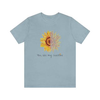 You are my Sunshine Unisex Jersey Short Sleeve Tee in Light Blue. Shown is the front showcasing a sunflower which is split down the middle and half is made out of paw prints. Underneath is the phrase "You are my Sunshine" . Back of shirt features the Sunflower Benefit Beagle Logo.