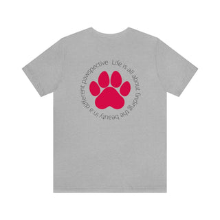 Different Pawspectives Unisex Jersey Short Sleeve Tee in Athletic Heather. Shown is the back of shirt featuring a large colorful pawprint with the the phrase "Life is all about finding the beauty in a different pawspective" circled around it. The Benefit Beagle Logo is located in the top corner on the front of shirt.