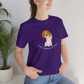 Easily Distracted Unisex Jersey Short Sleeve Tee in Team Purple. Shown is front design featuring a dog waving with the saying "Easily Distracted by Dogs" below it. The back of shirt has the classic Benefit Beagle Logo.