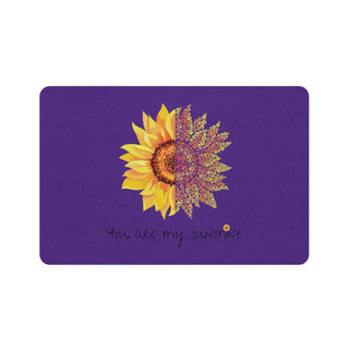 You are my Sunshine Pet Food Mat in Purple. The design features a sunflower which is split down the middle and half is made out of paw prints. There is the phrase "You are my Sunshine" at the bottom of the design.