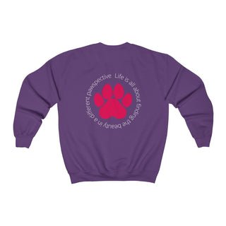 Different Pawspective Unisex Crewneck Sweatshirt in Purple. Shown is the back of shirt featuring a large colorful pawprint with the the phrase "Life is all about finding the beauty in a different pawspective" circled around it. The Benefit Beagle Logo is located in the top corner on the front of shirt.