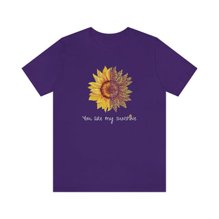 You are my Sunshine Unisex Jersey Short Sleeve Tee in Team Purple. Shown is the front showcasing a sunflower which is split down the middle and half is made out of paw prints. Underneath is the phrase "You are my Sunshine" . Back of shirt features the Sunflower Benefit Beagle Logo.