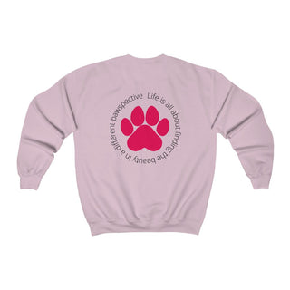 Different Pawspective Unisex Crewneck Sweatshirt in Light Pink. Shown is the back of shirt featuring a large colorful pawprint with the the phrase "Life is all about finding the beauty in a different pawspective" circled around it. The Benefit Beagle Logo is located in the top corner on the front of shirt.