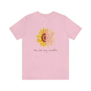 You are my Sunshine Unisex Jersey Short Sleeve Tee in Pink. Shown is the front showcasing a sunflower which is split down the middle and half is made out of paw prints. Underneath is the phrase "You are my Sunshine" . Back of shirt features the Sunflower Benefit Beagle Logo.