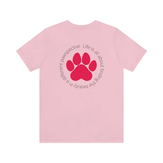 Different Pawspectives Unisex Jersey Short Sleeve Tee in Pink. Shown is the back of shirt featuring a large colorful pawprint with the the phrase "Life is all about finding the beauty in a different pawspective" circled around it. The Benefit Beagle Logo is located in the top corner on the front of shirt.