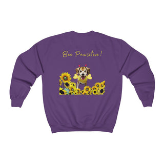 Bee Pawsitive Unisex Crewneck Sweatshirt shirt in Purple. Shown is back of shirt showcasing a dog dressed as as bee in a a field of sunflowers with the phrase "Bee Pawsitive!" above it. The front features the Bee Pawsitive Benefit Beagle Logo.