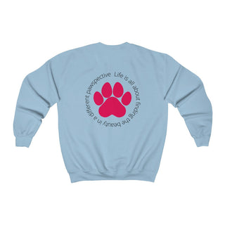 Different Pawspective Unisex Crewneck Sweatshirt in Light Blue. Shown is the back of shirt featuring a large colorful pawprint with the the phrase "Life is all about finding the beauty in a different pawspective" circled around it. The Benefit Beagle Logo is located in the top corner on the front of shirt.