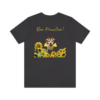 Bee Pawsitive Unisex Jersey Short Sleeve Tee shirt in Dark Grey. Shown is back of shirt showcasing a dog dressed as as bee in a a field of sunflowers with the phrase "Bee Pawsitive!" above it. The front features the Bee Pawsitive Benefit Beagle Logo.