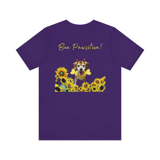 Bee Pawsitive Unisex Jersey Short Sleeve Tee shirt in Team Purple. Shown is back of shirt showcasing a dog dressed as as bee in a a field of sunflowers with the phrase "Bee Pawsitive!" above it. The front features the Bee Pawsitive Benefit Beagle Logo.