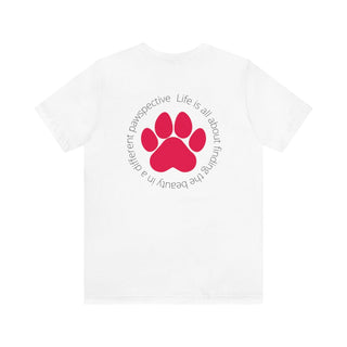 Different Pawspectives Unisex Jersey Short Sleeve Tee in White. Shown is the back of shirt featuring a large colorful pawprint with the the phrase "Life is all about finding the beauty in a different pawspective" circled around it. The Benefit Beagle Logo is located in the top corner on the front of shirt.