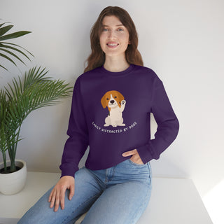 Easily Distracted Unisex Heavy Blend Crewneck Sweatshirt in Purple. Shown is front design featuring a dog waving with the saying "Easily Distracted by Dogs" below it. The back of shirt has the classic Benefit Beagle Logo.