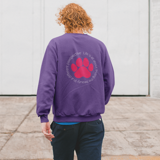 Different Pawspective Unisex Crewneck Sweatshirt in Purple. Shown is the back of shirt featuring a large colorful pawprint with the the phrase "Life is all about finding the beauty in a different pawspective" circled around it. The Benefit Beagle Logo is located in the top corner on the front of shirt.