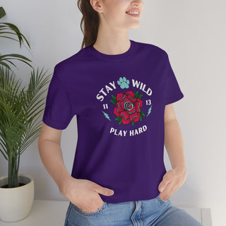 Stay Wild Unisex Premium Tee in Team Purple. Shown is front of Stay Wild Design features a tattoo style rose with the phrase "Stay Wild, Play Hard" around it. The back of shirt features the Stay Wild Benefit Beagle Logo Design.