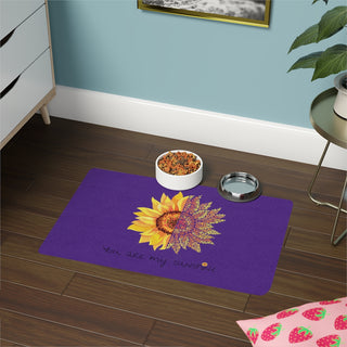 You are my Sunshine Pet Food Mat in Purple. The design features a sunflower which is split down the middle and half is made out of paw prints. There is the phrase "You are my Sunshine" at the bottom of the design.